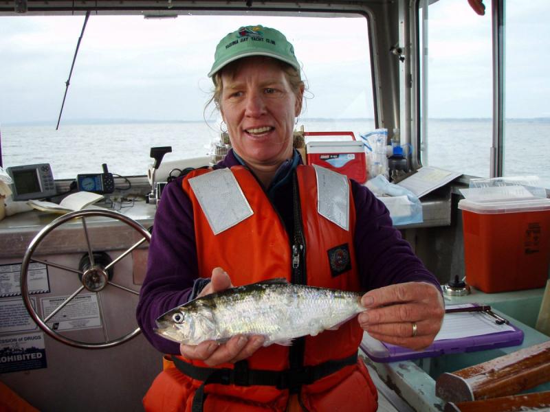 woman on a vessel wearing a life vest holding a silver colored fish