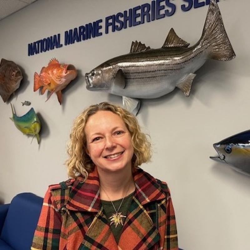 Headshot of Jenni Wallace standing in front of display fish and a NOAA Fisheries sign
