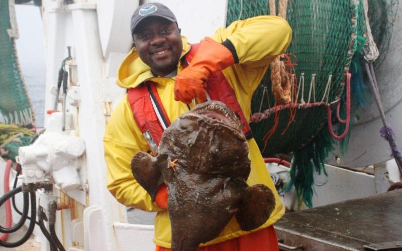 Calvin Alexander in yellow and orange gear holding large monkfish.