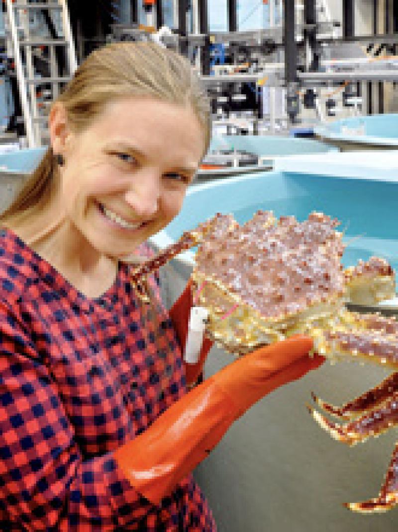 Smiling woman with checker shirt holding up a crab