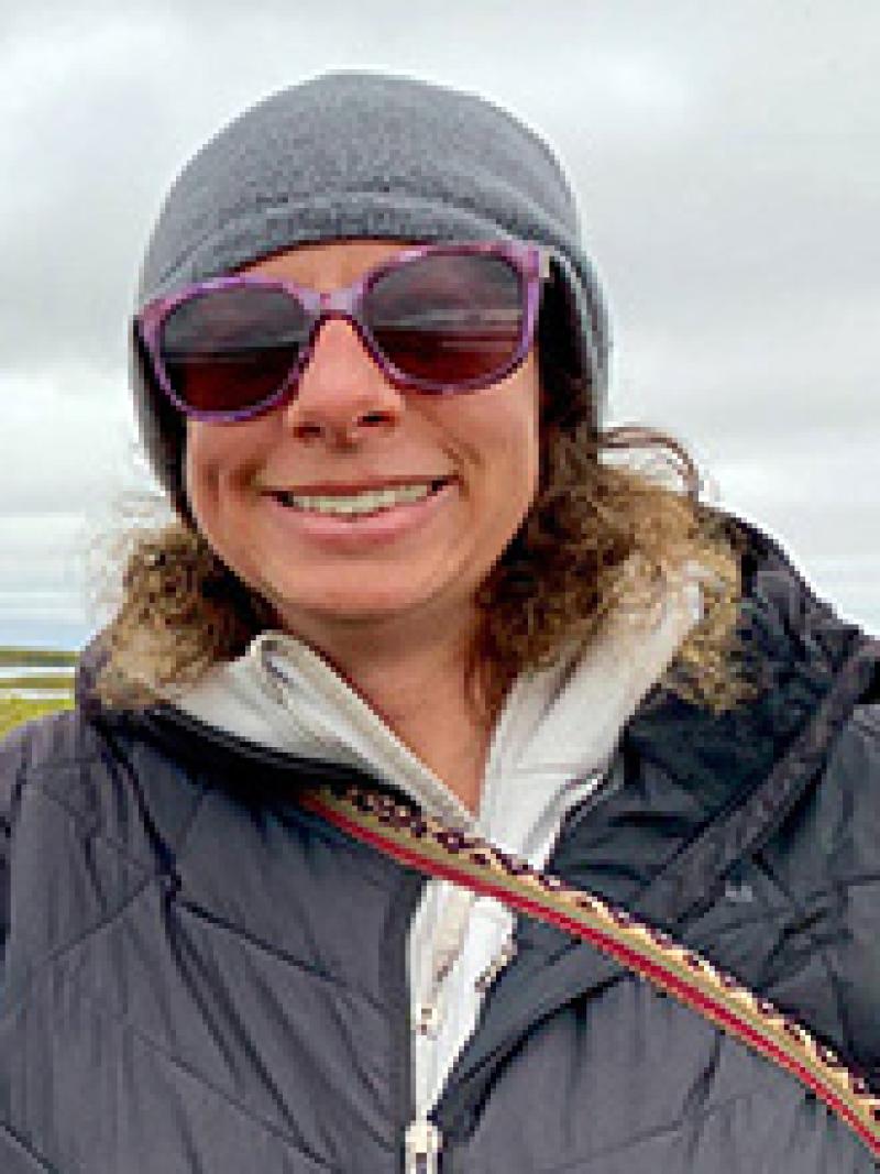 Woman with gray hat and glasses with landscape in background