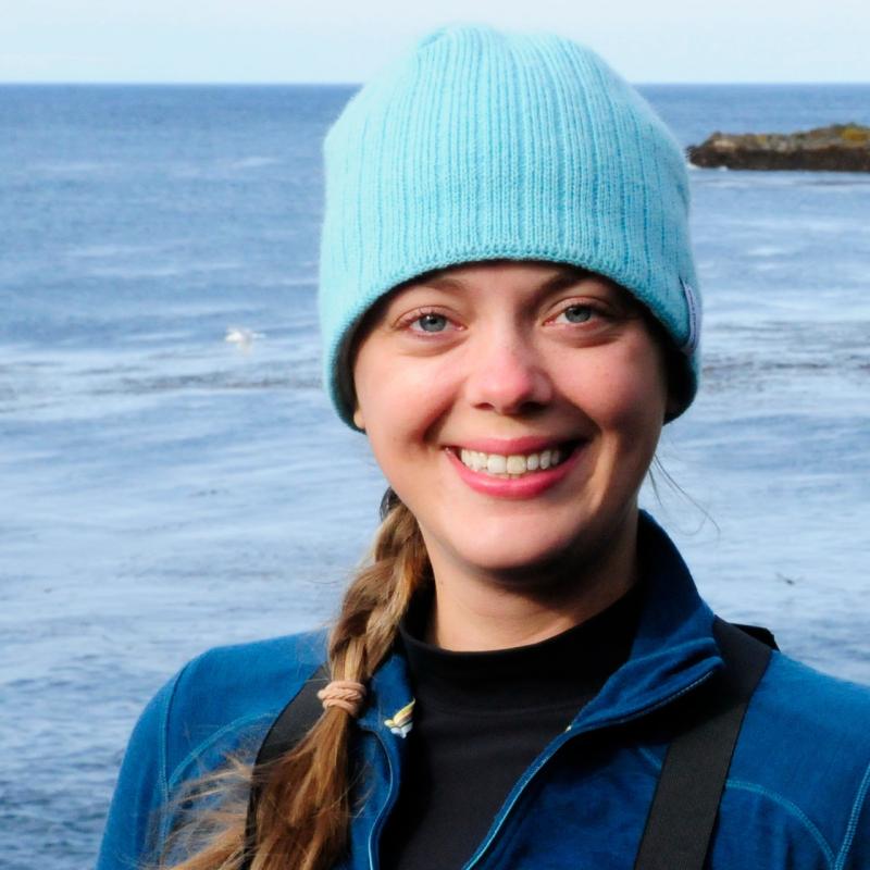 Woman in blue beanie and coat with ocean in background. 