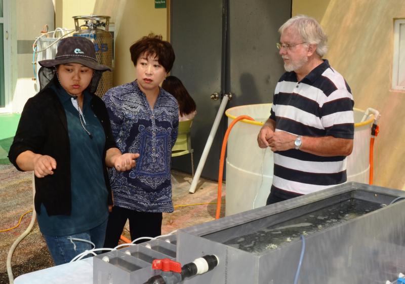 Scientist discussing experiments, silver tank in foreground.