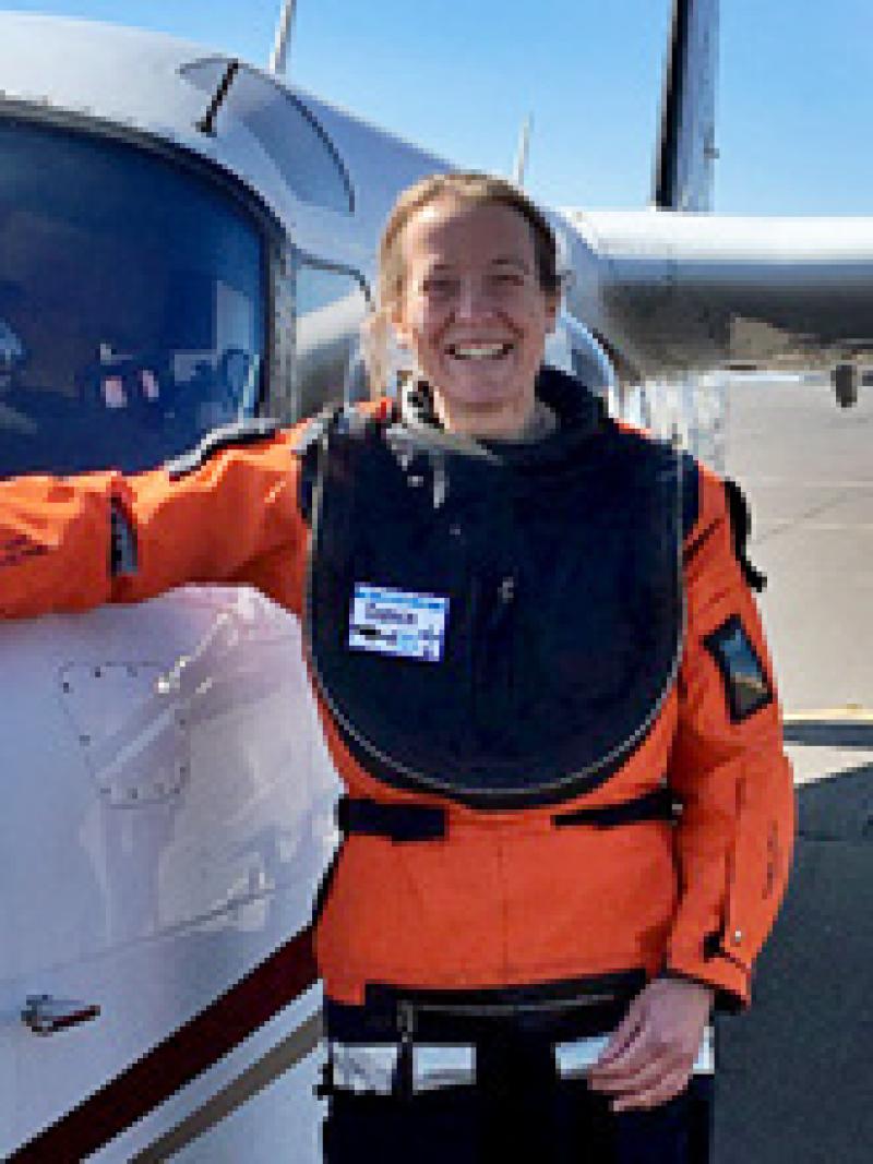 Woman with orange coat next to a plane 