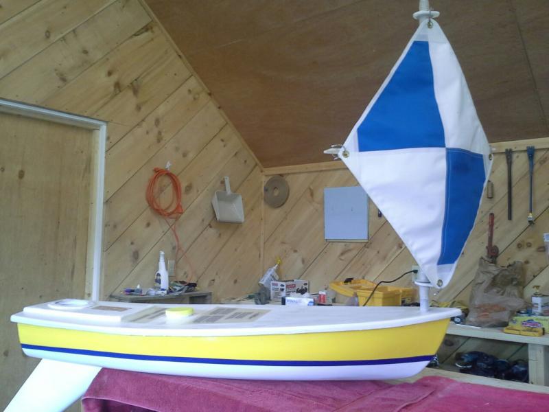 Yellow miniboat with blue and white sail on workbench.