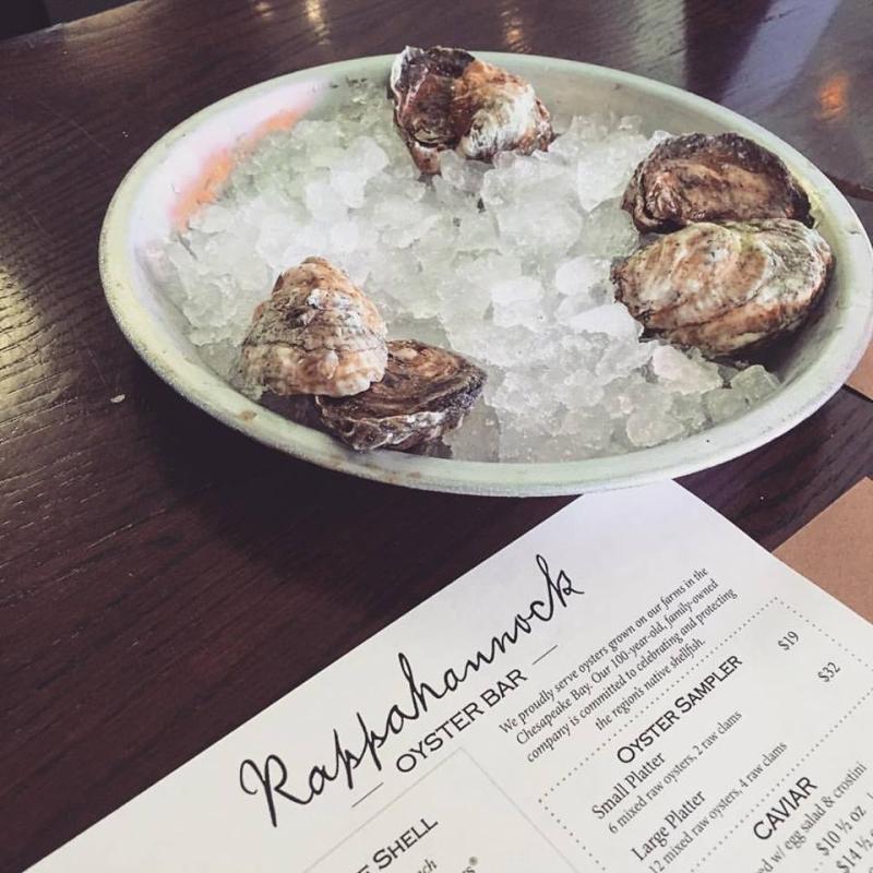 Raw oysters rest on a dish full of ice next to a Rappahannock Oyster Bar menu.