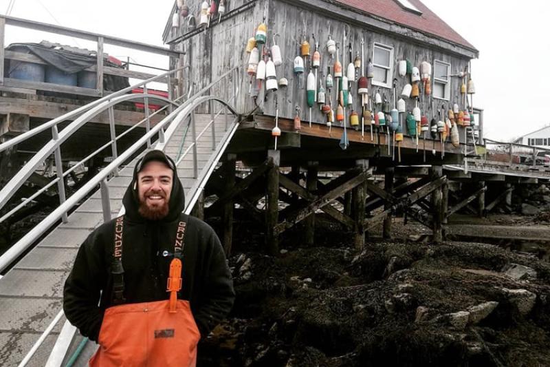 Zachary Fyke, in orange weather gear and black hoodie in front of lobster shack. 
