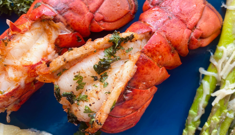 Two cooked lobster tails and a lemon on a blue background.